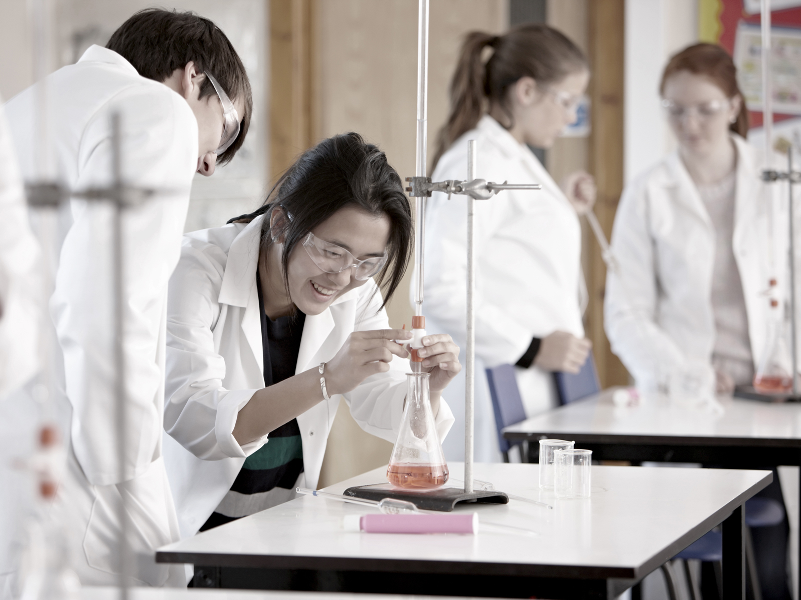 Three students under the supervision of a teacher watch clouds of steam coming out of a beaker Three students under the supervision of a teacher watch clouds of steam coming out of a beaker