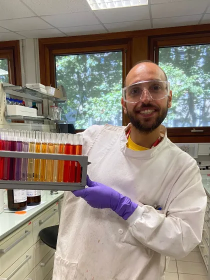 One of the PISCO Team in a lab coat and gloves holding test tubes with coloured liquids in