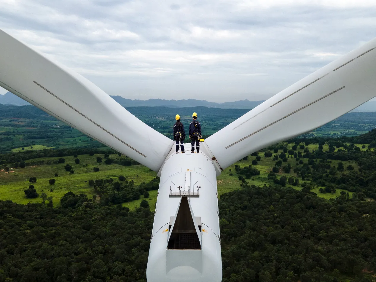 two people standing on top of a wind turbine looking out to the horizon