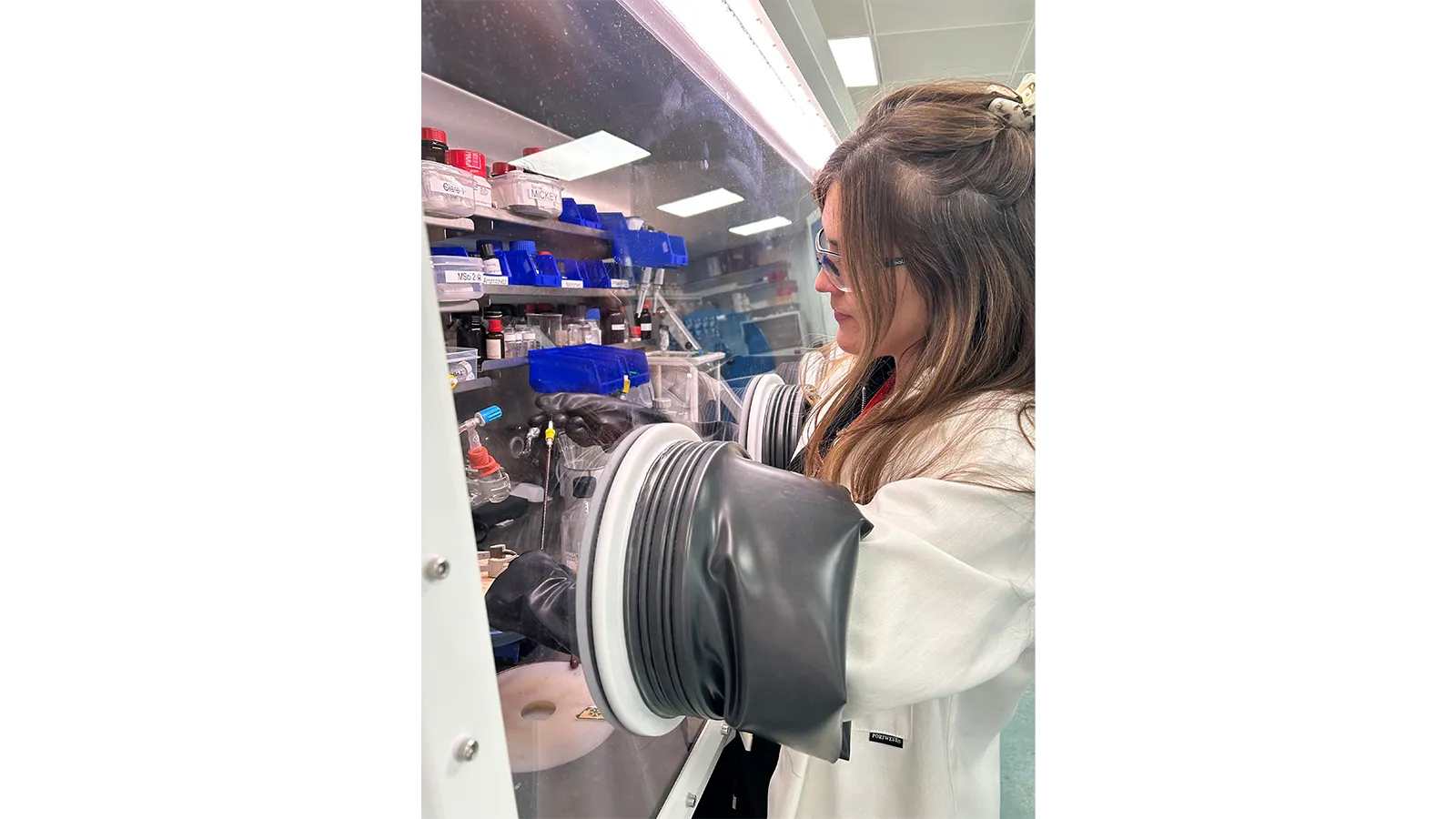 Dr Clare Bakewell wearing a white lab coat and using glove box