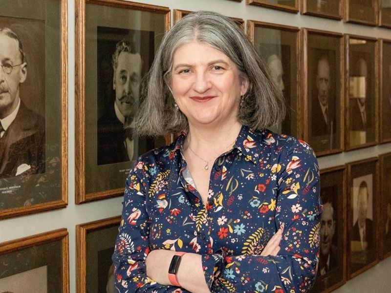 A head-and-shoulders picture of a smiling Dr Helen Pain in a floral blouse in front of a series of portrait pictures at Burlington House A head-and-shoulders picture of a smiling Dr Helen Pain in a floral blouse in front of a series of portrait pictures at Burlington House