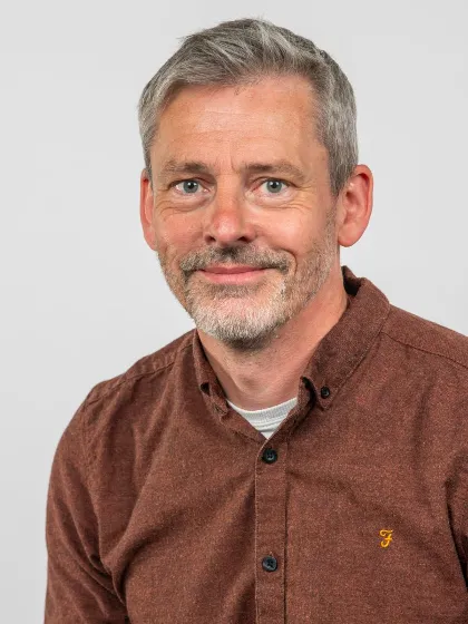 Professor Dave Adams with grey hair and beard and wearing brown shirt smiling - 900 x 1200